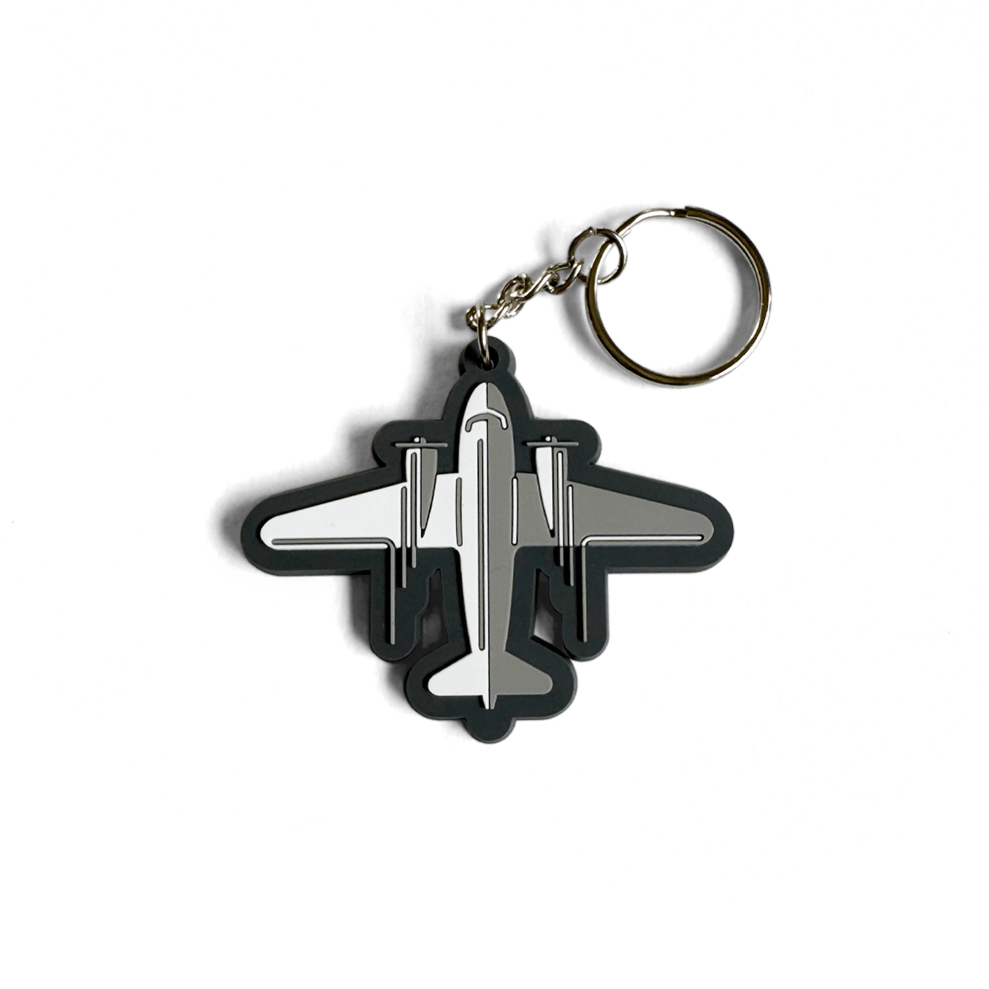 DC-3 Keychain featuring a stylized black and silver aircraft silhouette in rubber or PVC material, attached to a metal split ring. The plane design shows a top-down view with distinctive twin engines and straight wings characteristic of the classic DC-3 aircraft.