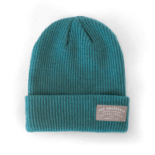 Load image into Gallery viewer, Knit Patch Beanie in vibrant teal color with ribbed texture, featuring a folded cuff and gray branded patch. Warm winter hat with classic beanie styling and vertical knit pattern, perfect for showing Kansas City pride.
